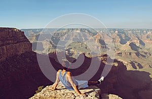 Young man sitting on the edge of Grand Canyon in sunglasses