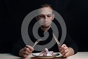 a young man is sitting at an empty table with a plate of raw chicken on it, the concept of a bad Thanksgiving