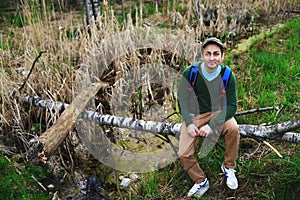 Young man sitting on a fallen tree trunk amongst trees enjoying nature