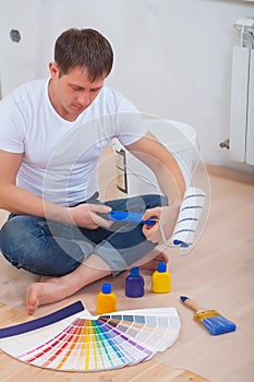 A young man sitting on floor holding paint roller