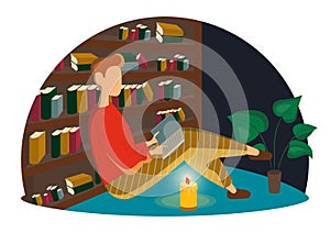 Young man sitting on the floor in library and reading book. Leisure activity, repose and relaxation. Candle lights the