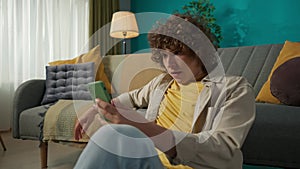 Young man sitting on the floor in the living room and watching a movie on his smartphone