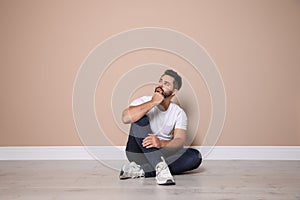 Young man sitting on floor near beige wall indoors