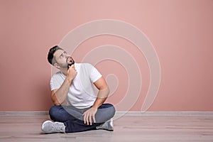 Young man sitting on floor near pink wall indoors. Space for text