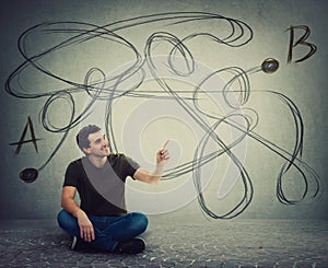 Young man sitting on the floor pointing forefinger finding the correct way from point A to point B. Solving problem, find solution