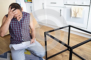 Young man sitting on the floor and reading instructions for assembling furniture at home.