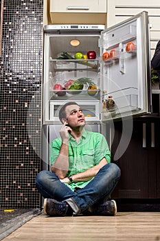 Young Man Sitting In Front Of Fridge