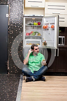 Young Man Sitting In Front Of Fridge