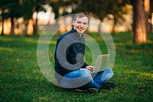 Young man sitting on the grass in the park and work on laptop