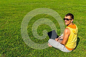 Young man sitting on the grass and working with laptop