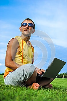 Young man sitting on the grass and working with laptop