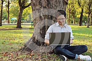 Young man sitting on green grass and enjoying with laptop in the park