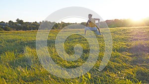 Young man sitting at green grass in the meadow and doing yoga exercise. Muscular guy stretching his body at nature