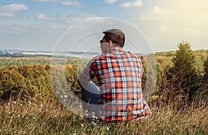 Young man sitting on a hill enjoying scenery. Concept of travel and freedom