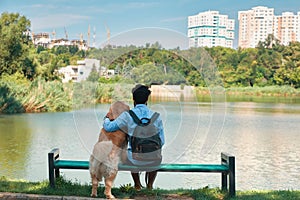 Young man sitting with his dog on the chair in the park, enjoyin