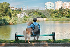 Young man sitting with his dog on the chair in the park, enjoyin