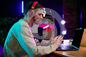 Young man sitting in home office in headphones, with microphone and laptop, recording online podcast. Social media