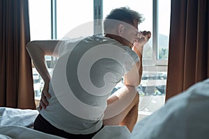 Young man sitting indoor on the bed feeling ache in his back