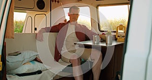 Young man sitting inside his camper van among corn field