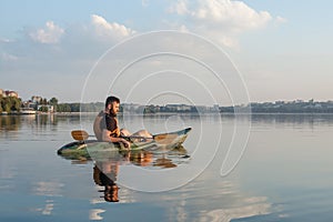 Young man sitting on kayak and having rest on the lake on a summer morning