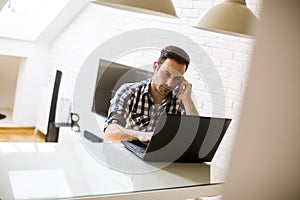 Young man sitting on kitchen desk at home and using laptop and mobile phone