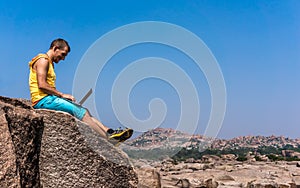 Young man sitting on the mountain with beautiful view and working with laptop