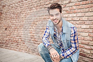 Young man sitting near a brick wall