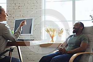 Young man sitting in office during the job interview with female employee, boss or HR-manager, talking, thinking, looks