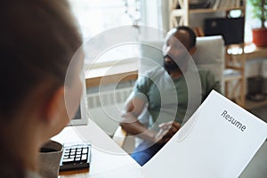 Young man sitting in office during the job interview with female employee, boss or HR-manager, talking, thinking, looks