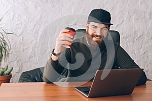 Young man sitting in office lookig at laptop and drinking coffee
