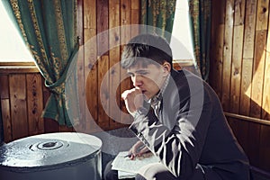 young man is sitting in an old rare railway car writing notes warming his hands at the stove
