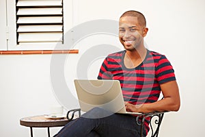 Young Man Sitting Outdoors With Laptop And Drinking Coffee