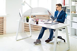 A young man is sitting with a phone in his hands at a table in the office.