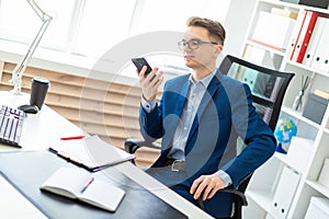 A young man is sitting with a phone in his hands at a table in the office.