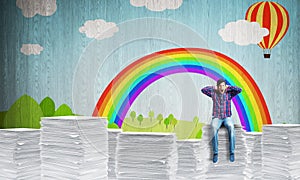 Young man sitting on pile of paper documents.