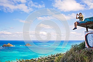 Young man sitting on pillbox over looking Lanikai taking a cell