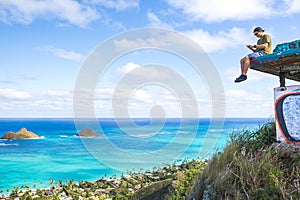 Young man sitting on pillbox over looking Lanikai texting on a c