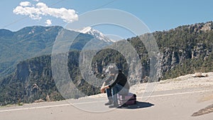 Young man  sitting on  purple suitcase sunny day