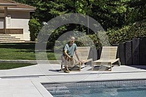 Young man sitting relaxed on a sun lounger in his garden pool on a hot summer day