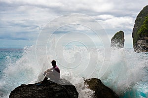 Young man sitting on the rock with the sea waves breaking in front