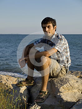 Young man sitting on rocks near sea during sunset