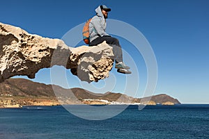 Young man sitting on sculpted rock structure, Los Escullos, Spain