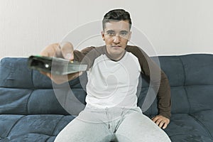 Young man sitting on sofa with expression of emotion with TV contro in hands. with his cell phone photo