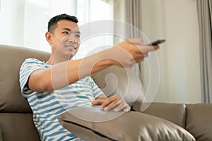 Young man sitting on sofa holding remote control and watching TV in living room at home