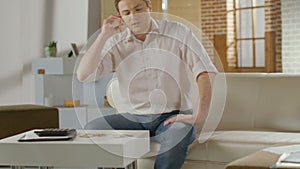 Young man sitting on sofa at home, having phone conversation