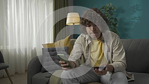 Young man sitting on the sofa in the living room with a smartphone and credit card in hands HDR BT2020 HLG Material.