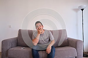 Young man sitting on a sofa yawning. Fatigue and tiredness concepts