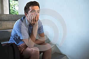 A young man is sitting on the stairs and sad. He lost the keys to the apartment,