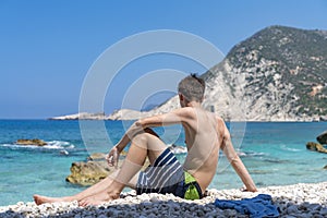 Young man sitting at a stone beach