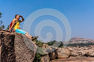 Young man sitting on the stone and enjoying the view after trekking